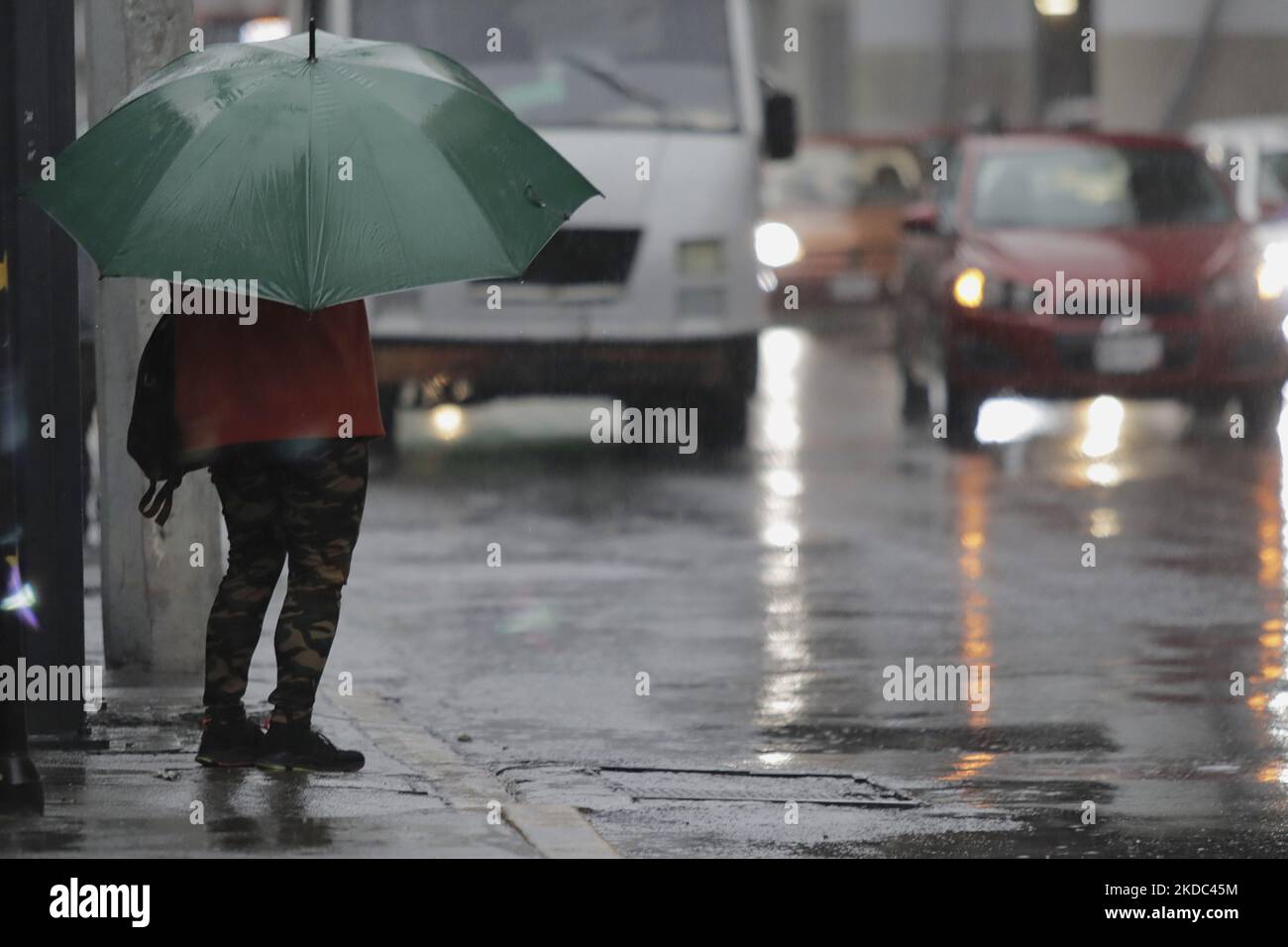 A person takes shelter from the rain with an umbrella while waiting for ...