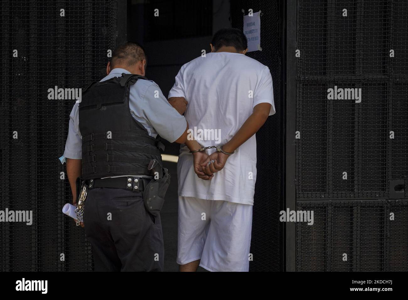 A police officer escorts an alleged gang member into a detention center on June 22, 2022 in San Salvador, El Salvador. The Salvadoran government through the Salvadoran Congress extended a state of emergency put in place to hit gang structures for the fourth month in a row as the government reports more than 41,000 alleged gang members captured (Photo by Camilo Freedman/NurPhoto) Stock Photo