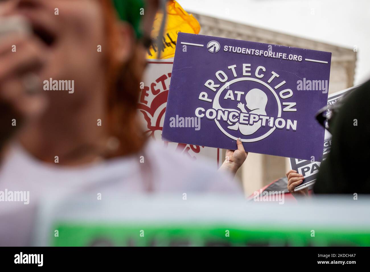 An anti-abortion sign is visible behind a pro-choice protester at the Supreme Court as demonstrators await its decision on Dobbs v. JWHO. A draft opinion leaked in May, 2022, indicating that the Court would overturn the federal right to abortion decided 49 years ago in Roe v. Wade, allowing each state to set its own laws. With the exception of Thomas, all of the conservative justices in the majority testified under oath in their confirmation hearings that they consider abortion access 'settled law.' (Photo by Allison Bailey/NurPhoto) Stock Photo