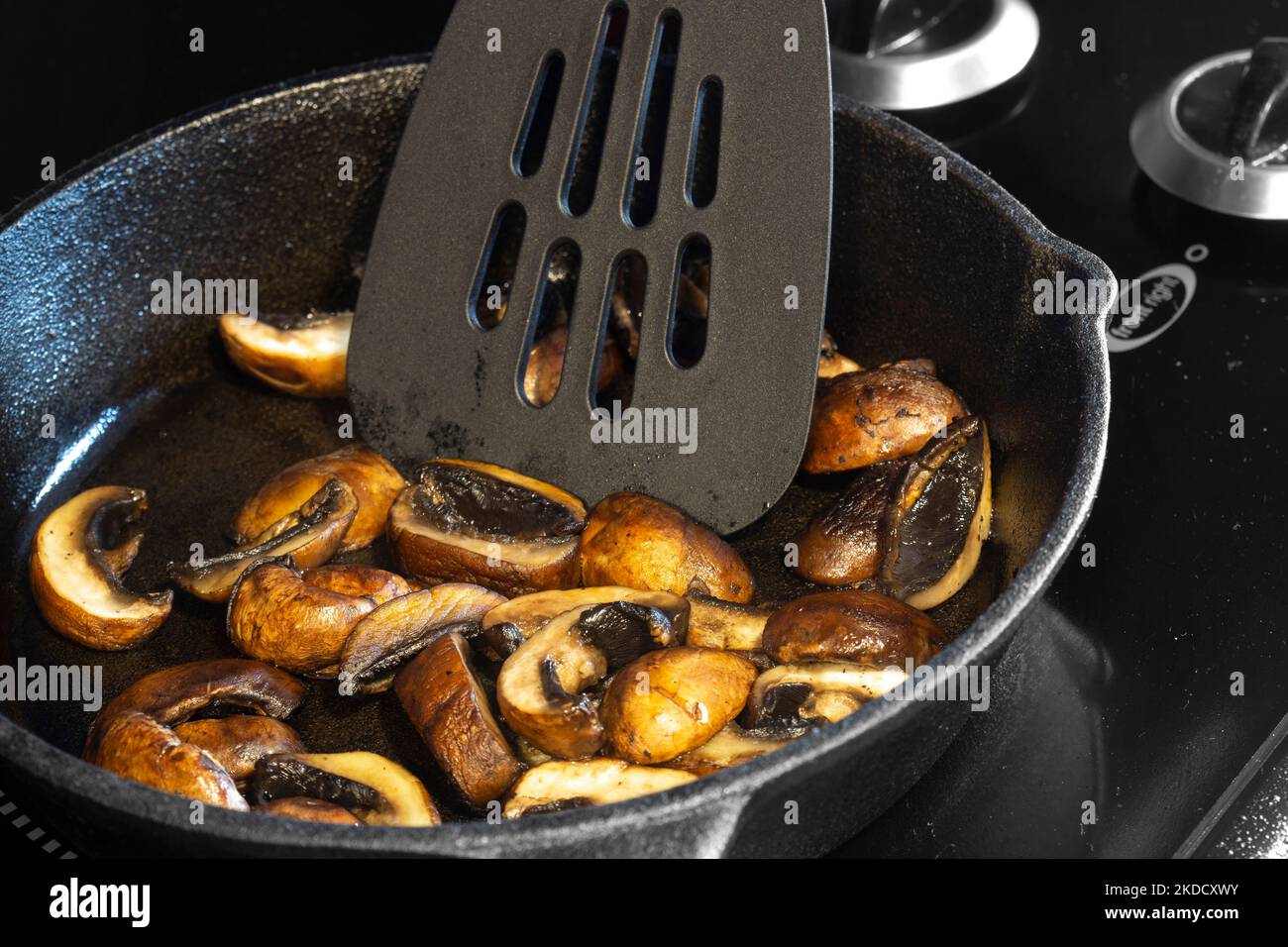 Frying chestnut mushrooms in a cast iron frying pan, on an electric hob stove Stock Photo