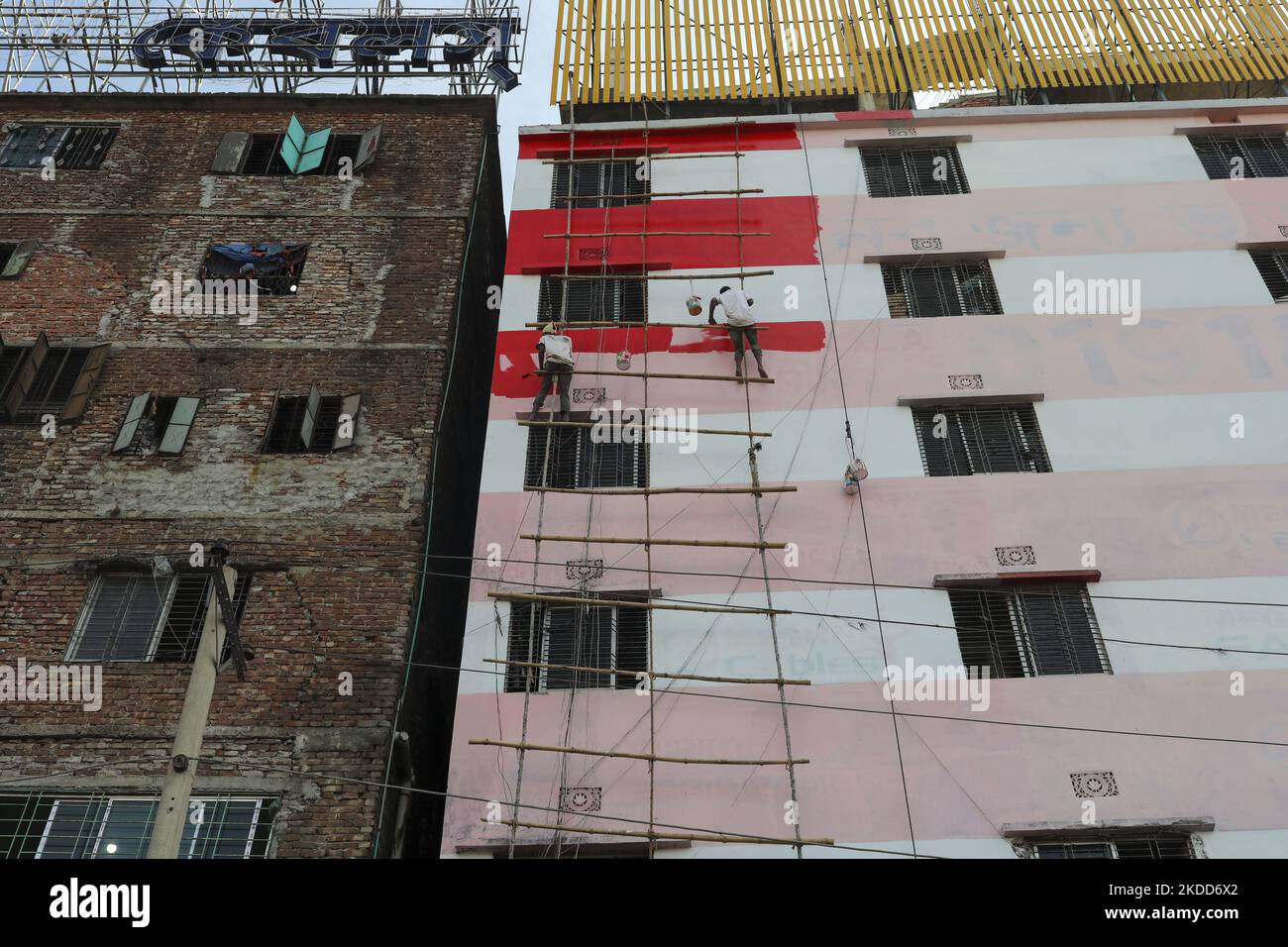 Two men without safety gears, paint a multi-storey building by hanging on a ladder made of rope and bamboo beside Buriganga river in Dhaka, Bangladesh on July 03, 2022. (Photo by Kazi Salahuddin Razu/NurPhoto) Stock Photo