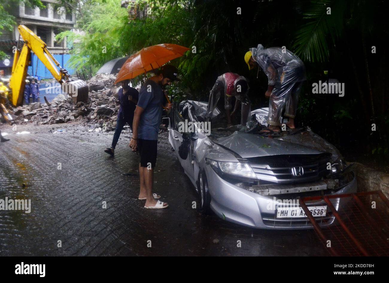 People looks into car damaged after a wall collapse during heavy