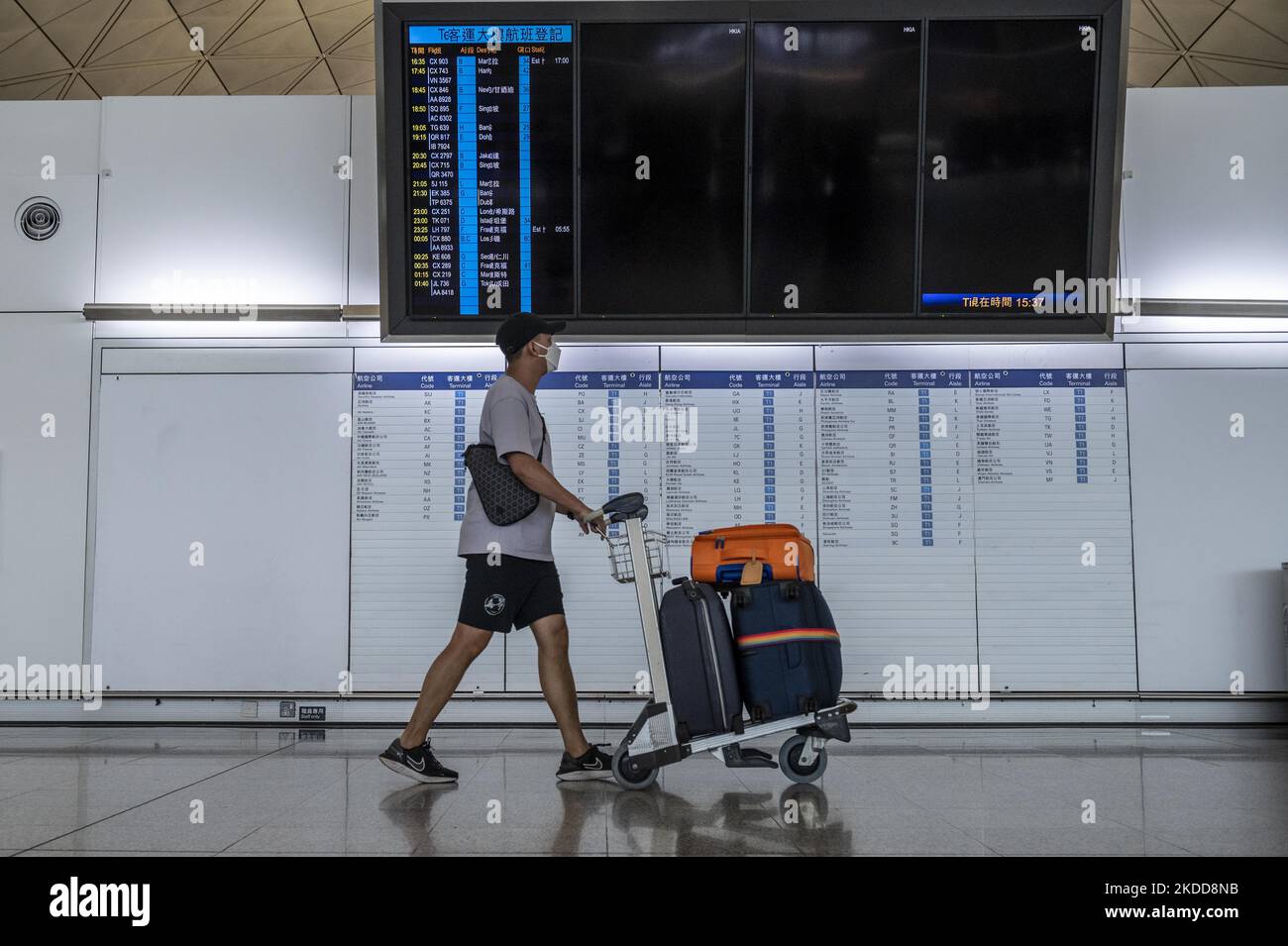 A Man pushing a luggage trolley walk pass an electronic flight display