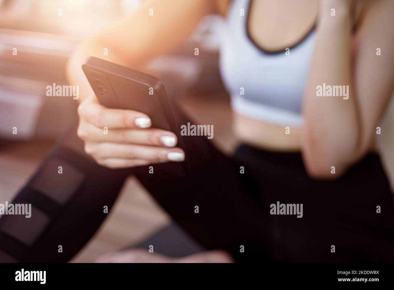 Young woman sitting on yoga mat after exercising, relaxing with smartphone and listening to music. Stock Photo