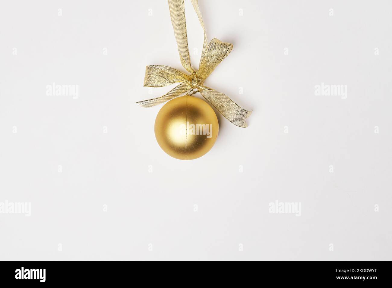 a golden christmas ball on a white background with a gold ribbon around it and a bow hanging from the top Stock Photo