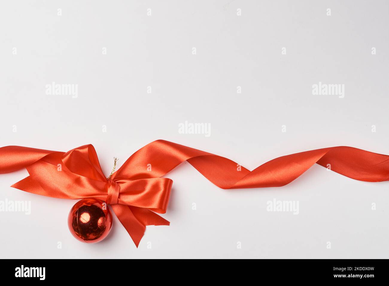 an orange ribbon on a white background with some red ribbons around it and a small bell in the corner to the bow is tied Stock Photo