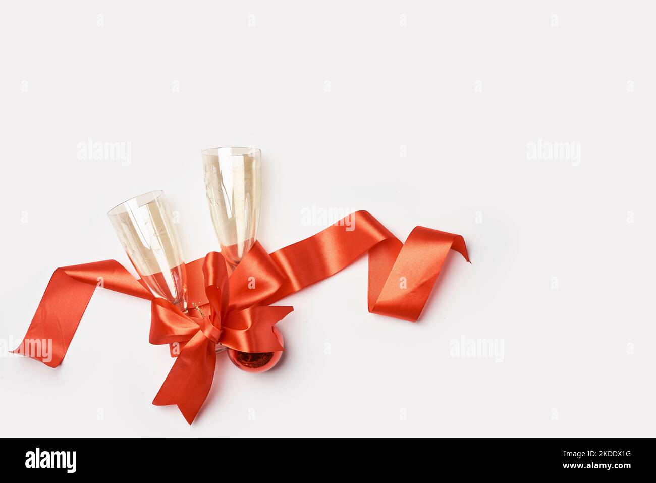 two champagne flutes wrapped in red satin ribbon on a white background with copy space for your text or message to be Stock Photo