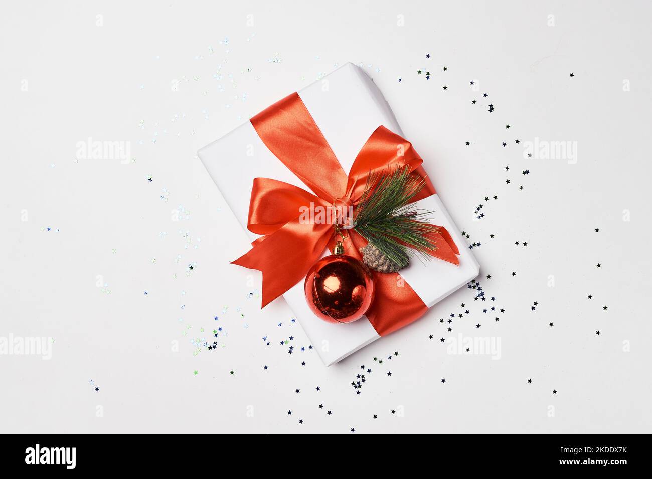 a christmas present wrapped in red ribbon and decorated with pine cones on a white surface surrounded by confe Stock Photo