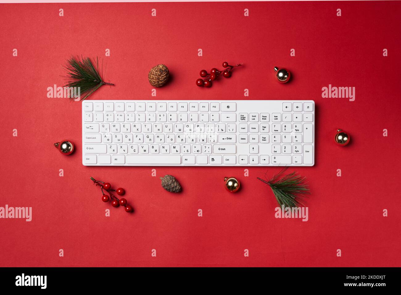 a computer keyboard on a red surface with christmas decorations around it and pine cones in the top right hand corner Stock Photo