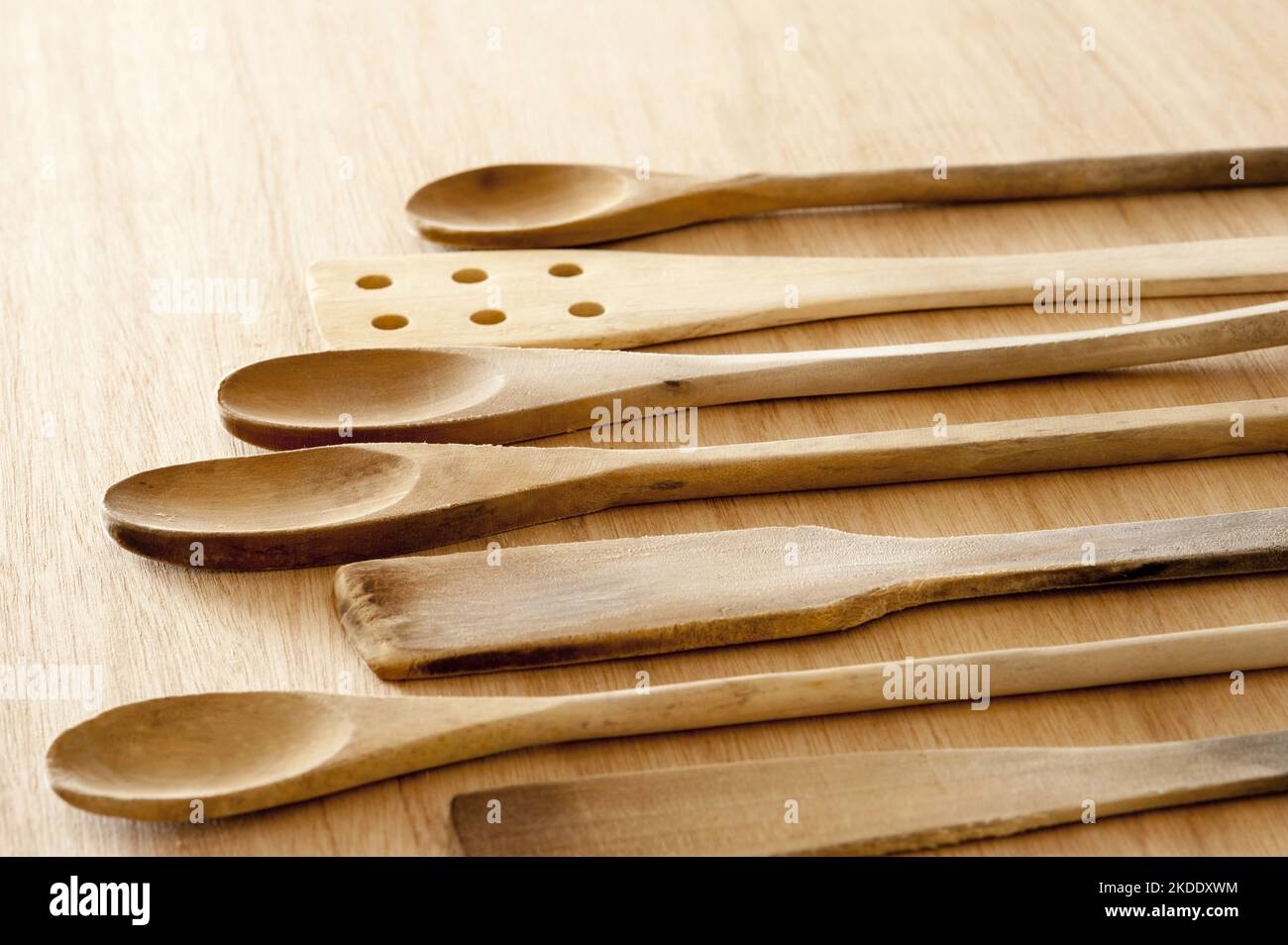 Selection of plain wooden rustic kitchen utensils with assorted spoons, spatulas and strainer in a receding low angle view on a wooden table Stock Photo