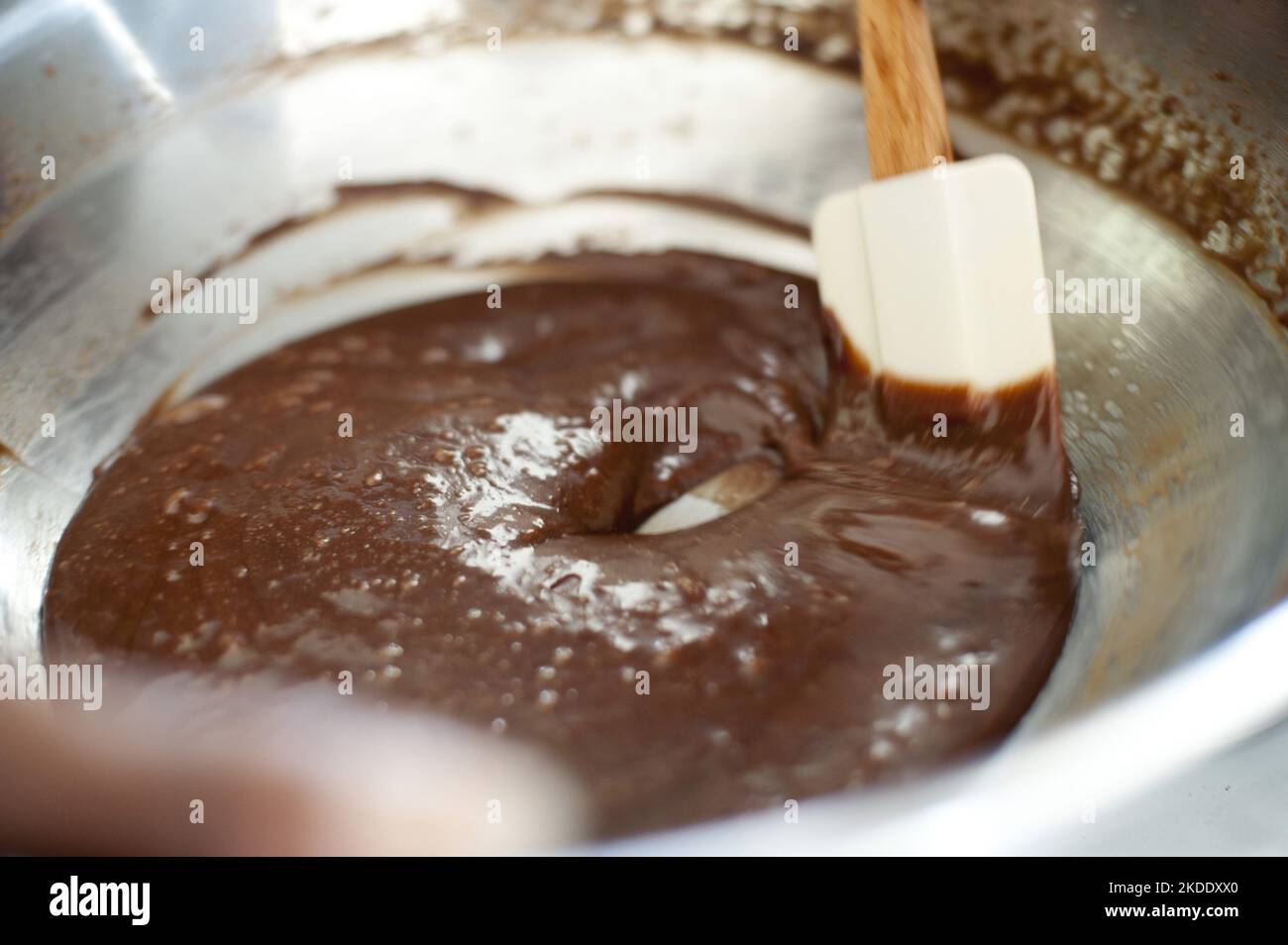 Cook making a bowl of chocolate icing cleaning around the edge of the mixing bowl with a rubber spatula Stock Photo
