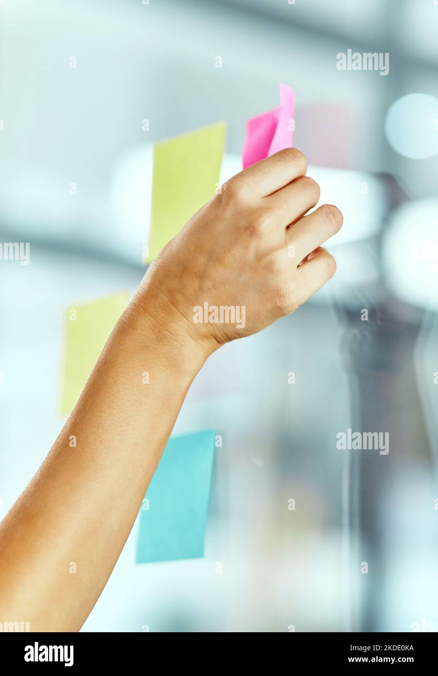 Let the brainstorming begin. a woman pasting notes on glass during a brainstorming session at work. Stock Photo