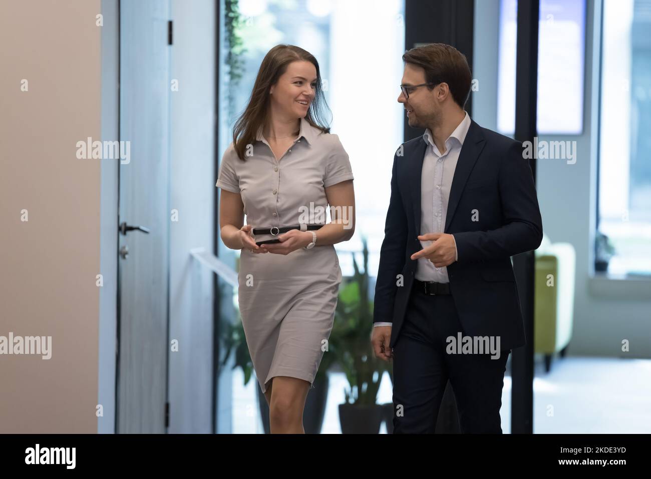 Young colleagues talking walking along modern hallway in office Stock Photo