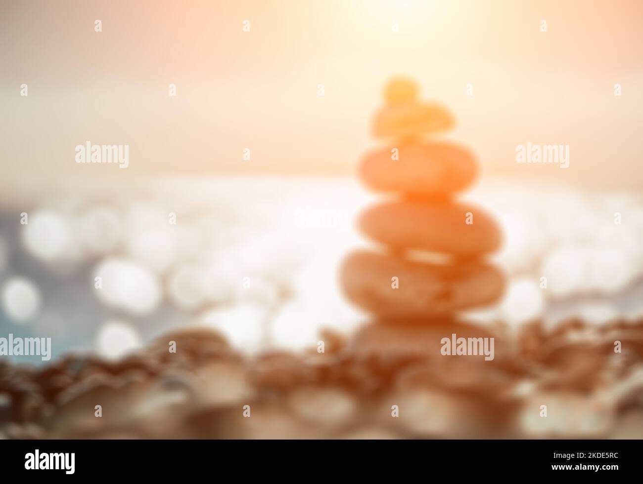 Abstract defocused blured background Balanced Pebbles Pyramid on the Beach on Sunny Day and Clear Sky at Sunset. Blue Sea on Background. Selective Stock Photo