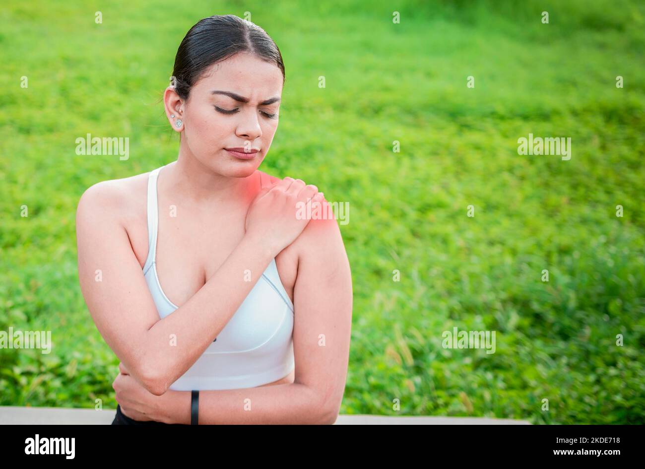 Young woman with shoulder pain sitting outside. Girl suffering from shoulder pain sitting