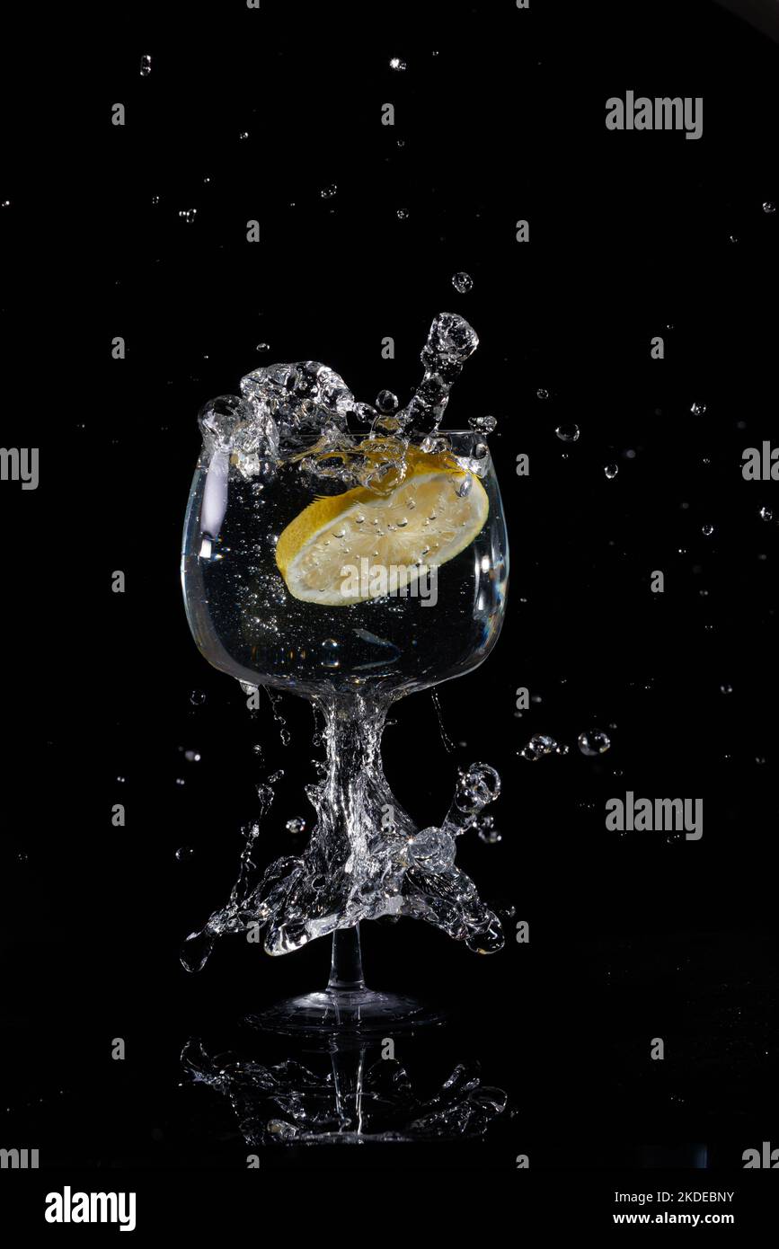 Lemon slice dropped into wine glass of water with splash on black