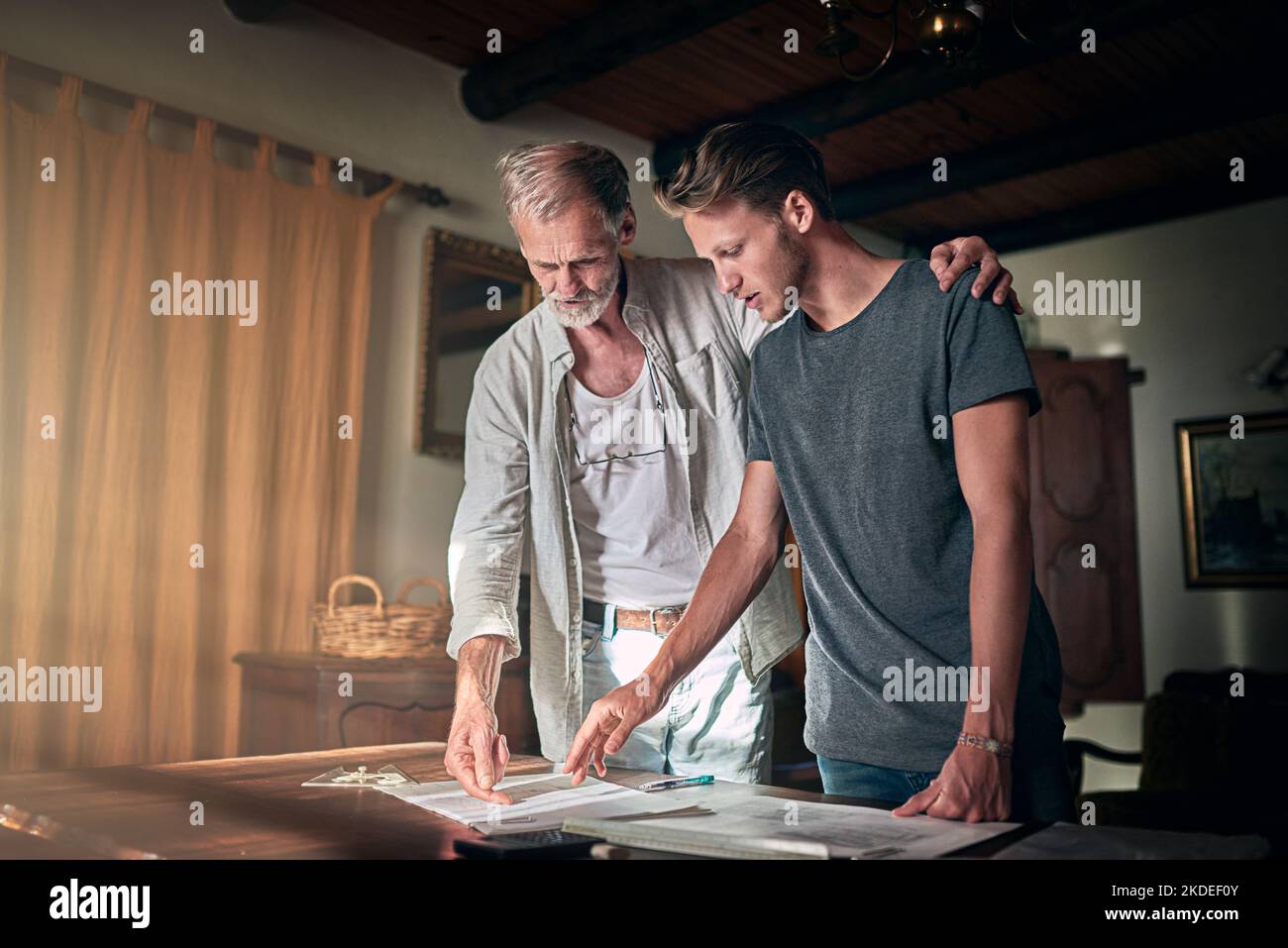 Dad is happy to help him perfect his design. a father and his son working on a design for their family business at home. Stock Photo