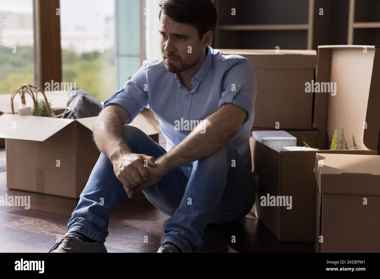 Depressed man sits on floor near boxes with stuff Stock Photo