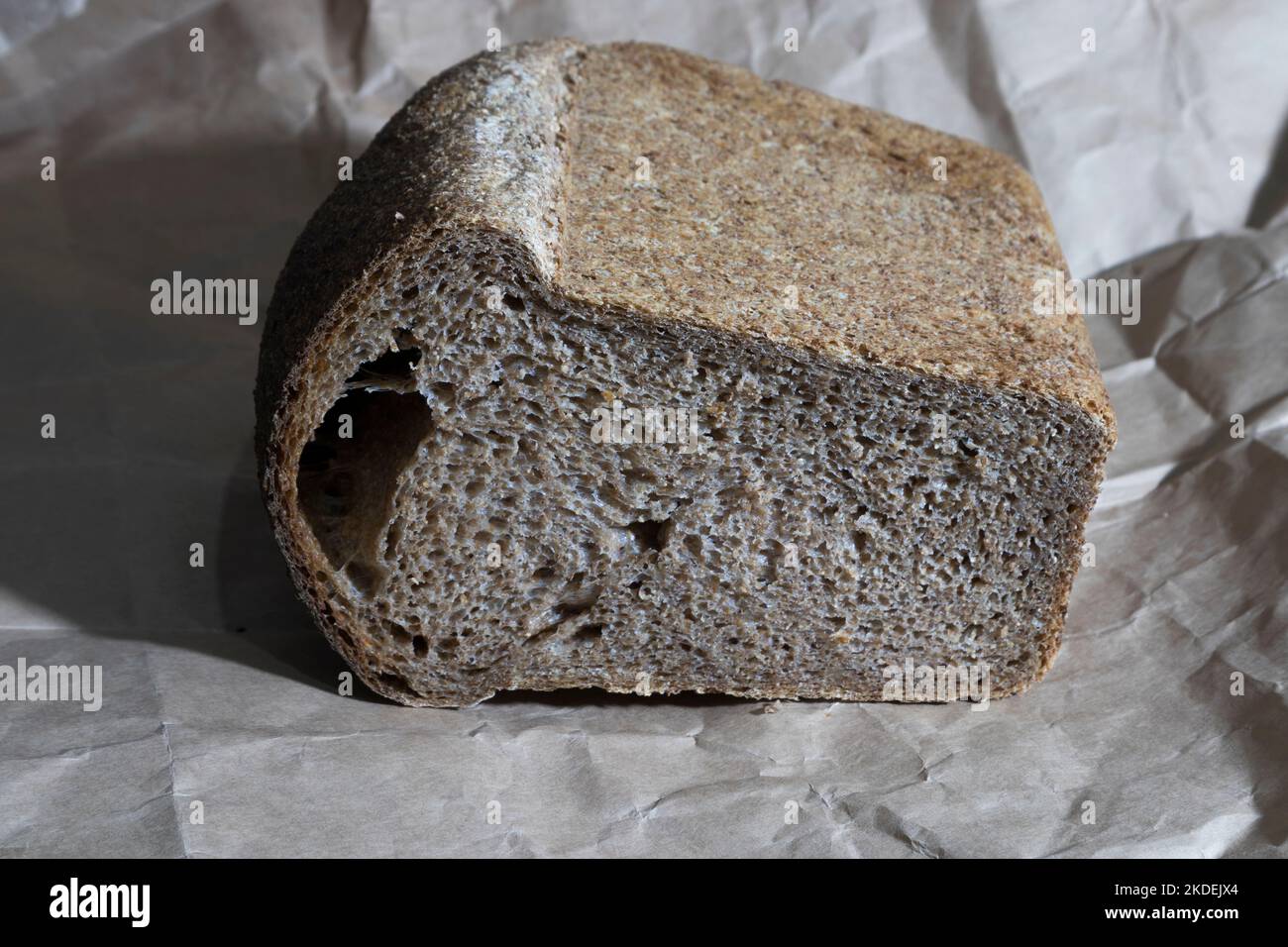 Bread baked from whole grain flour. For its baking, a collectible wheat variety Spelta neglectum was used. It is located on wrapping paper. Close-up. Stock Photo
