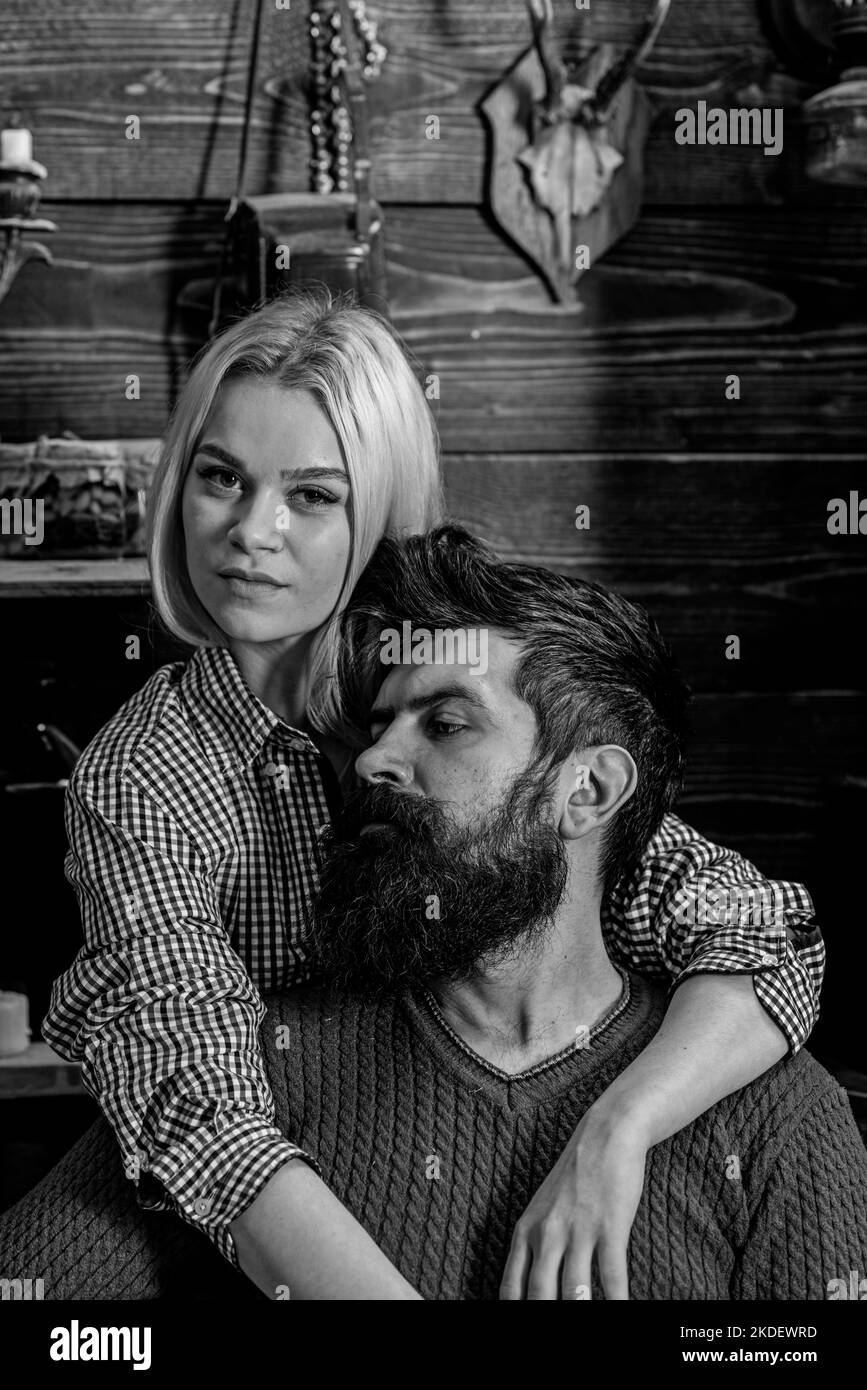Couple in wooden vintage interior enjoy rest. Lady and man with beard on dreamy faces hugs. Couple in love spend romantic evening in warm atmosphere Stock Photo
