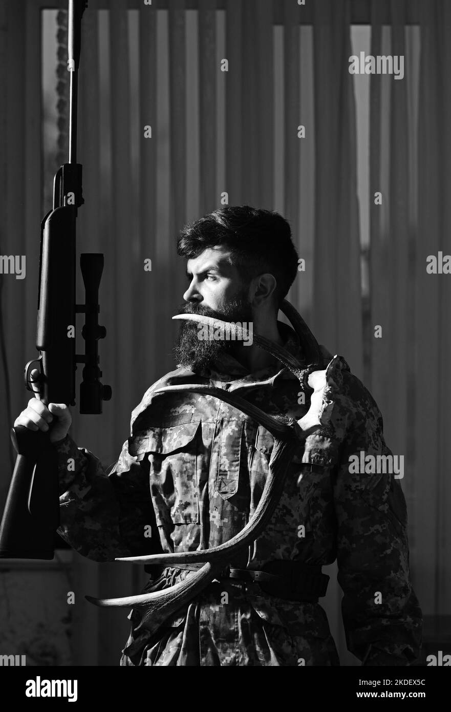 Gamekeeper concept. Man with beard wears camouflage clothing, curtains