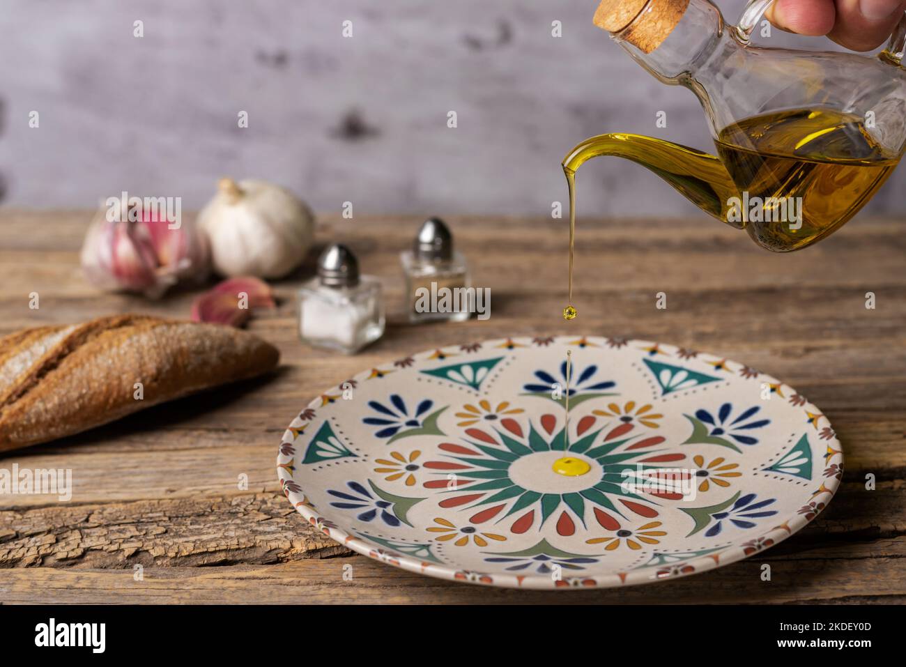 Extra virgin olive oil pouring from an oil can into a rustic round plate, on an old wooden table. Stock Photo