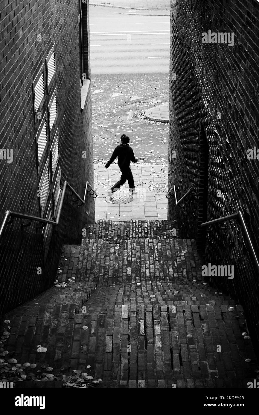 Old brick staircase in descending perspective with young urban person in motion blur walking on street in the background Stock Photo
