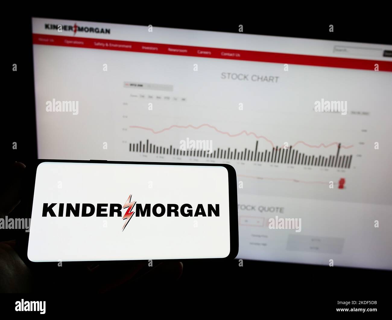 Person holding mobile phone with logo of American energy company Kinder Morgan Inc. on screen in front of web page. Focus on phone display. Stock Photo