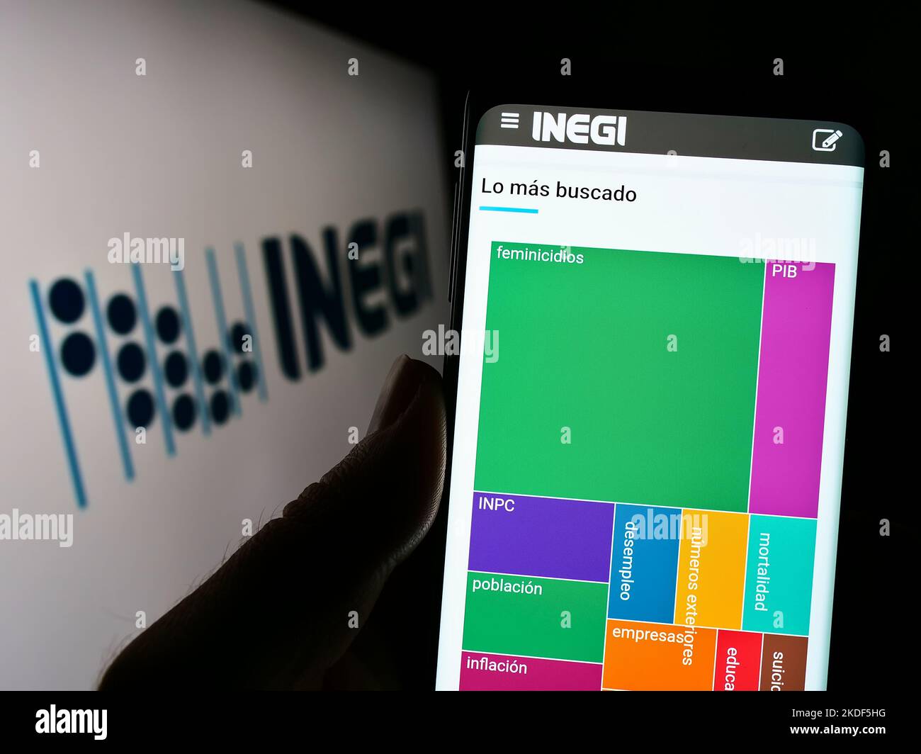 Person holding cellphone with website of Mexican statistics agency INEGI on screen in front of logo. Focus on center of phone display. Stock Photo
