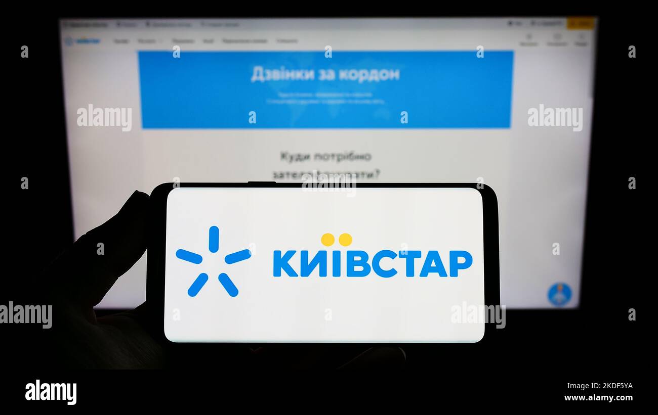 Person holding smartphone with logo of telecommunications company Kyivstar JSC on screen in front of website. Focus on phone display. Stock Photo