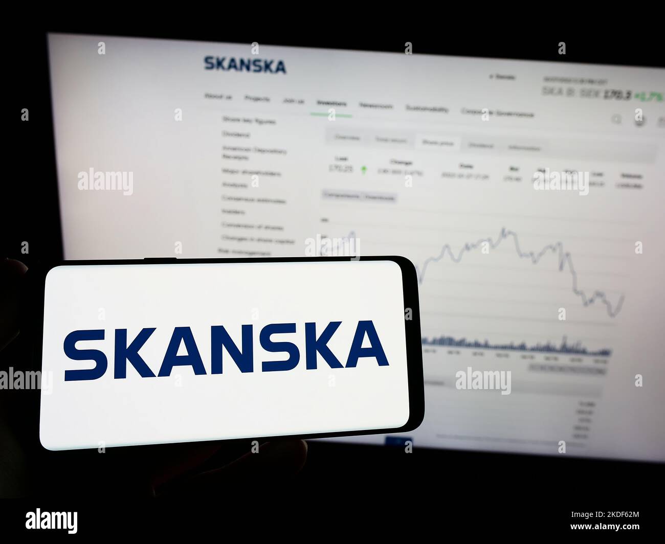 Person holding mobile phone with logo of Swedish construction company Skanska AB on screen in front of business web page. Focus on phone display. Stock Photo