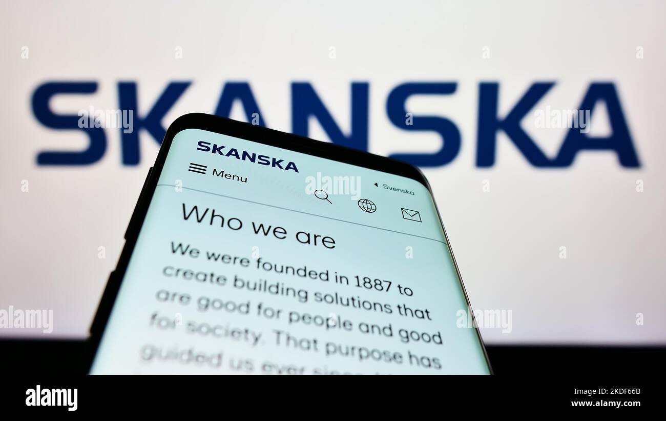 Mobile phone with webpage of Swedish construction company Skanska AB on screen in front of business logo. Focus on top-left of phone display. Stock Photo