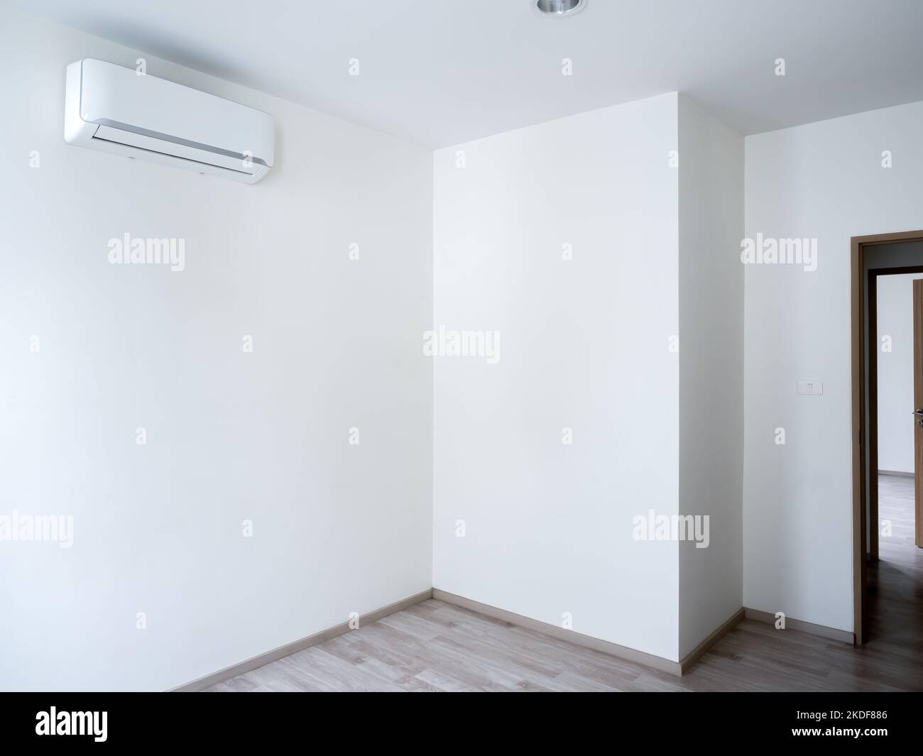 Blank white wall background with wall mounted air conditioner in the empty room near the wooden opened door near the window with copy space. White wal Stock Photo