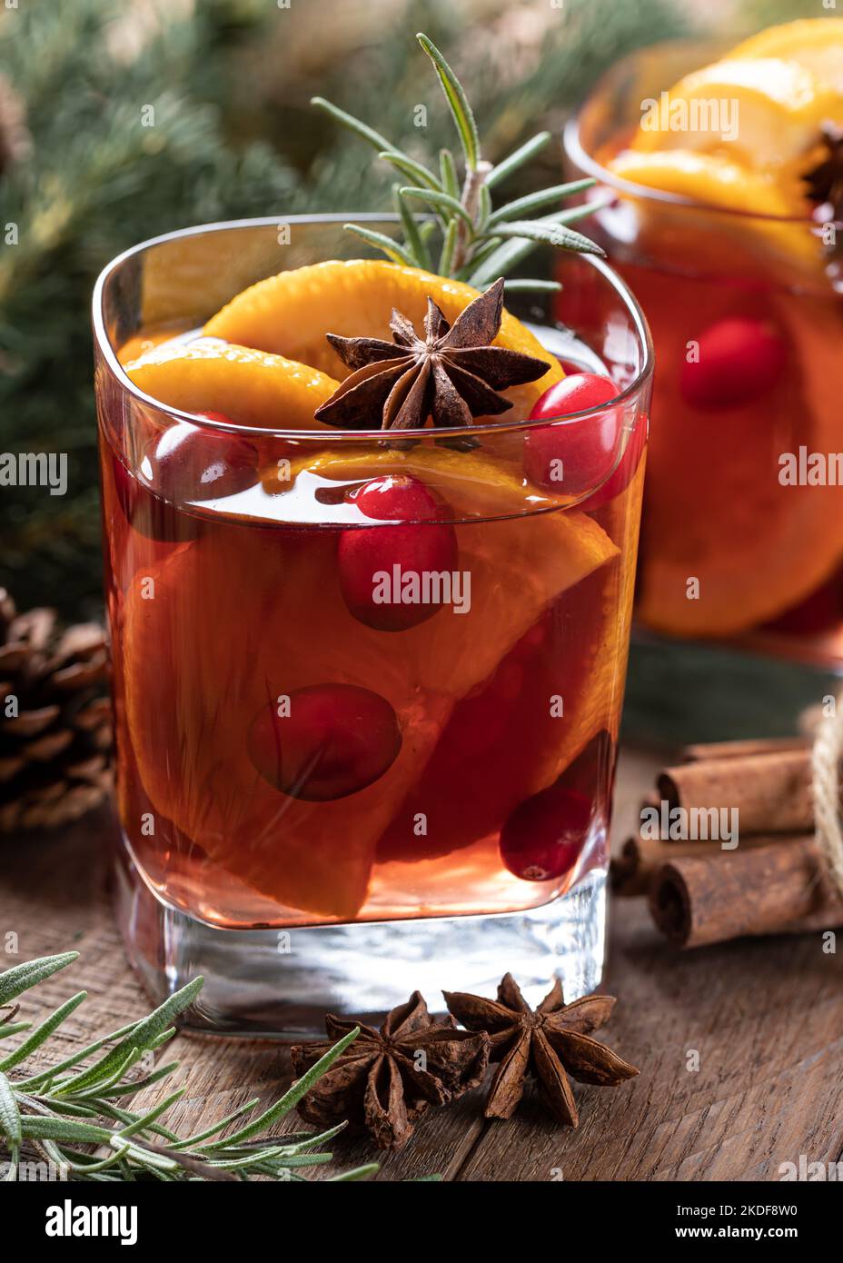 Mulled wine with orange slices, cranberries and spices on rustic wooden table with Christmas tree decoration in background Stock Photo