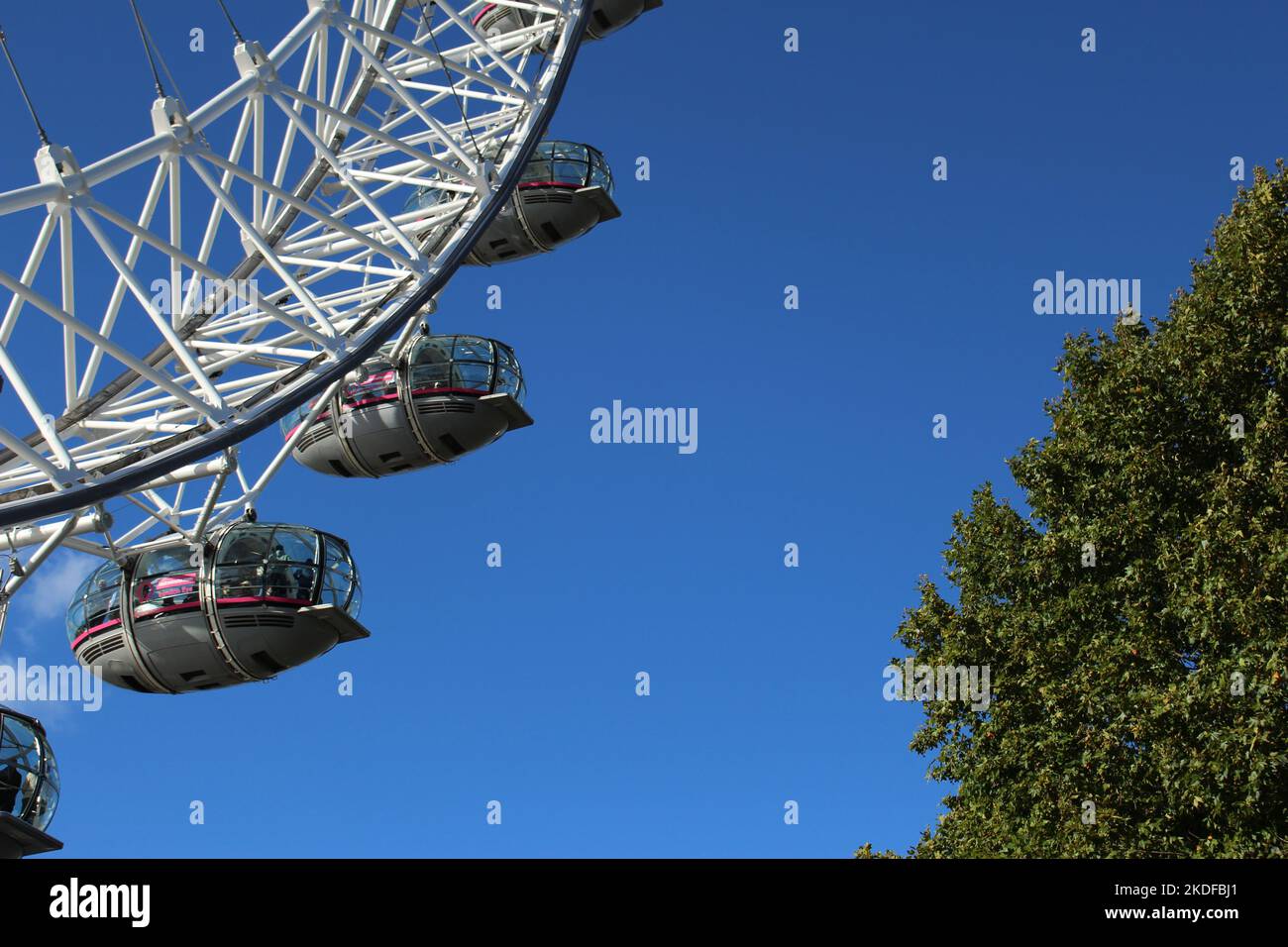 Tourists enjoy the Millennium Wheel on a sunny day. Close up picture of the carriages on the London Eye with greenery and blue sky background. Stock Photo