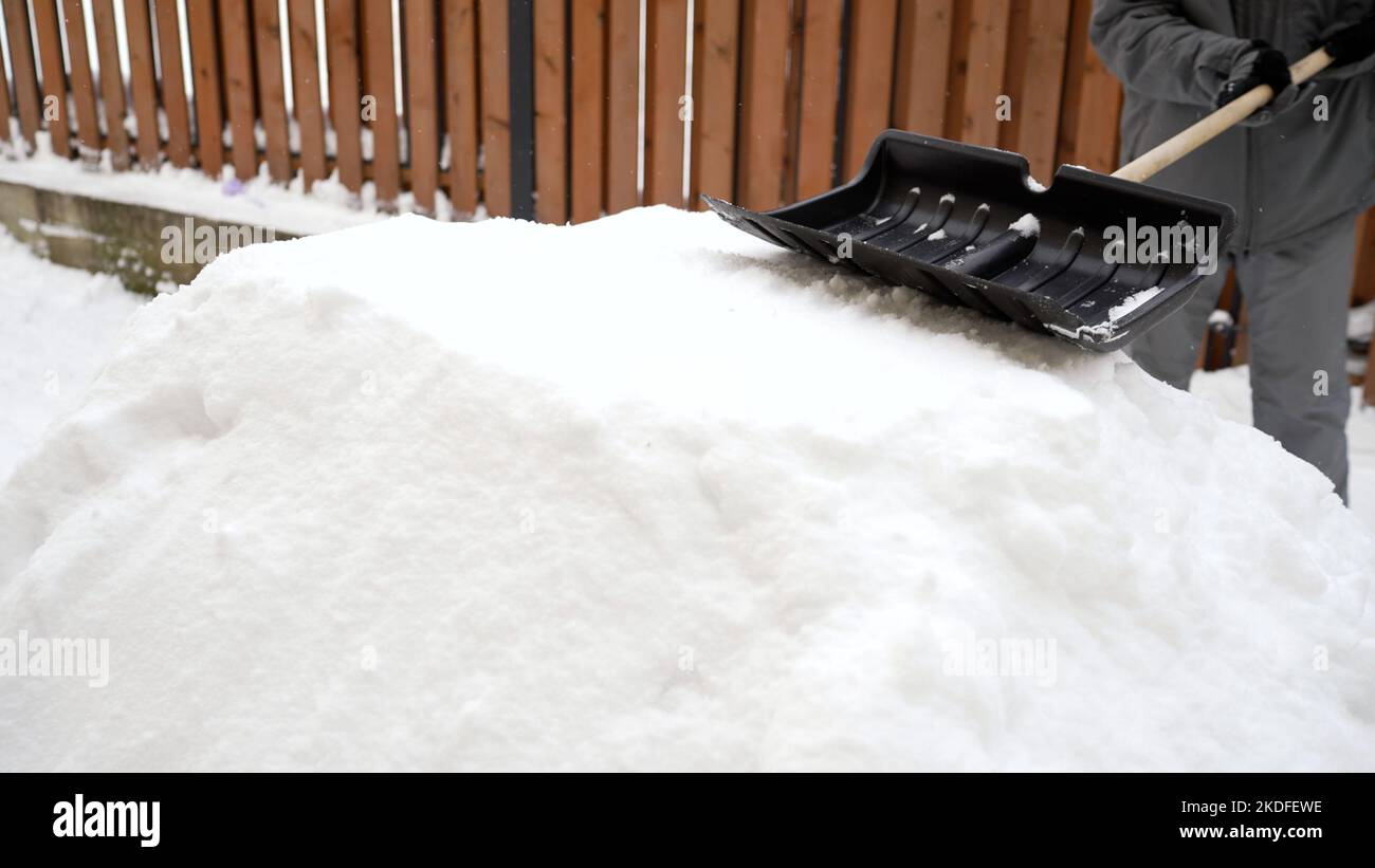 A man with a shovel in winter. Young man shoveling snow from the walking path in winter. A man with a shovel is building a children's slide from snow. Stock Photo