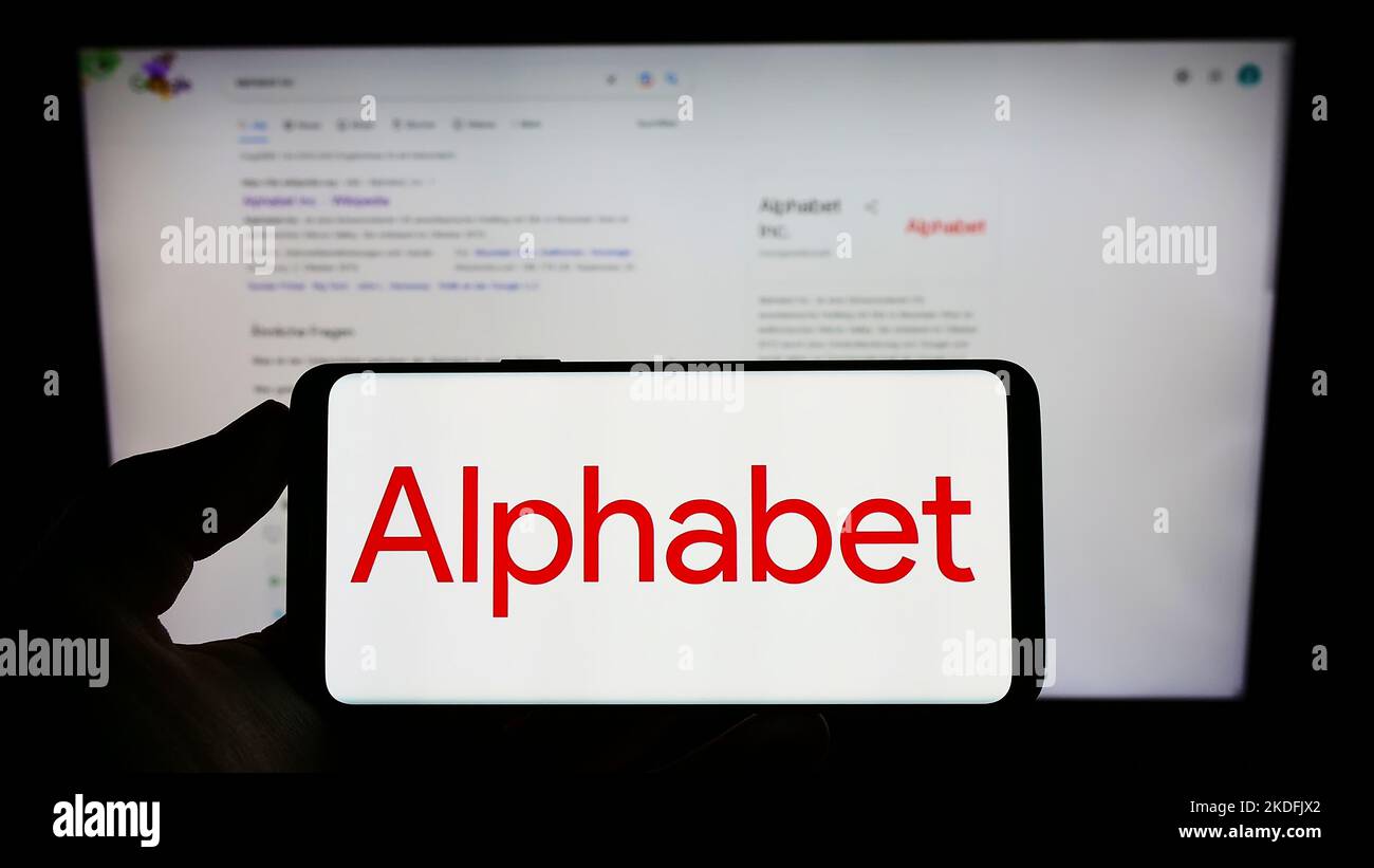 Person holding cellphone with logo of US holding company Alphabet Inc. (Google) on screen in front of business webpage. Focus on phone display. Stock Photo