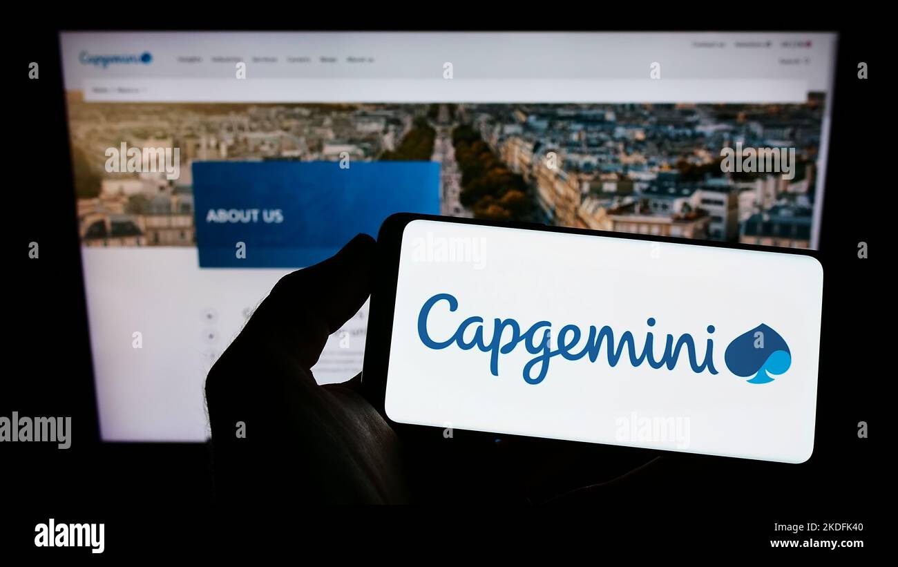 Person holding smartphone with logo of information technology company Capgemini SE on screen in front of website. Focus on phone display. Stock Photo