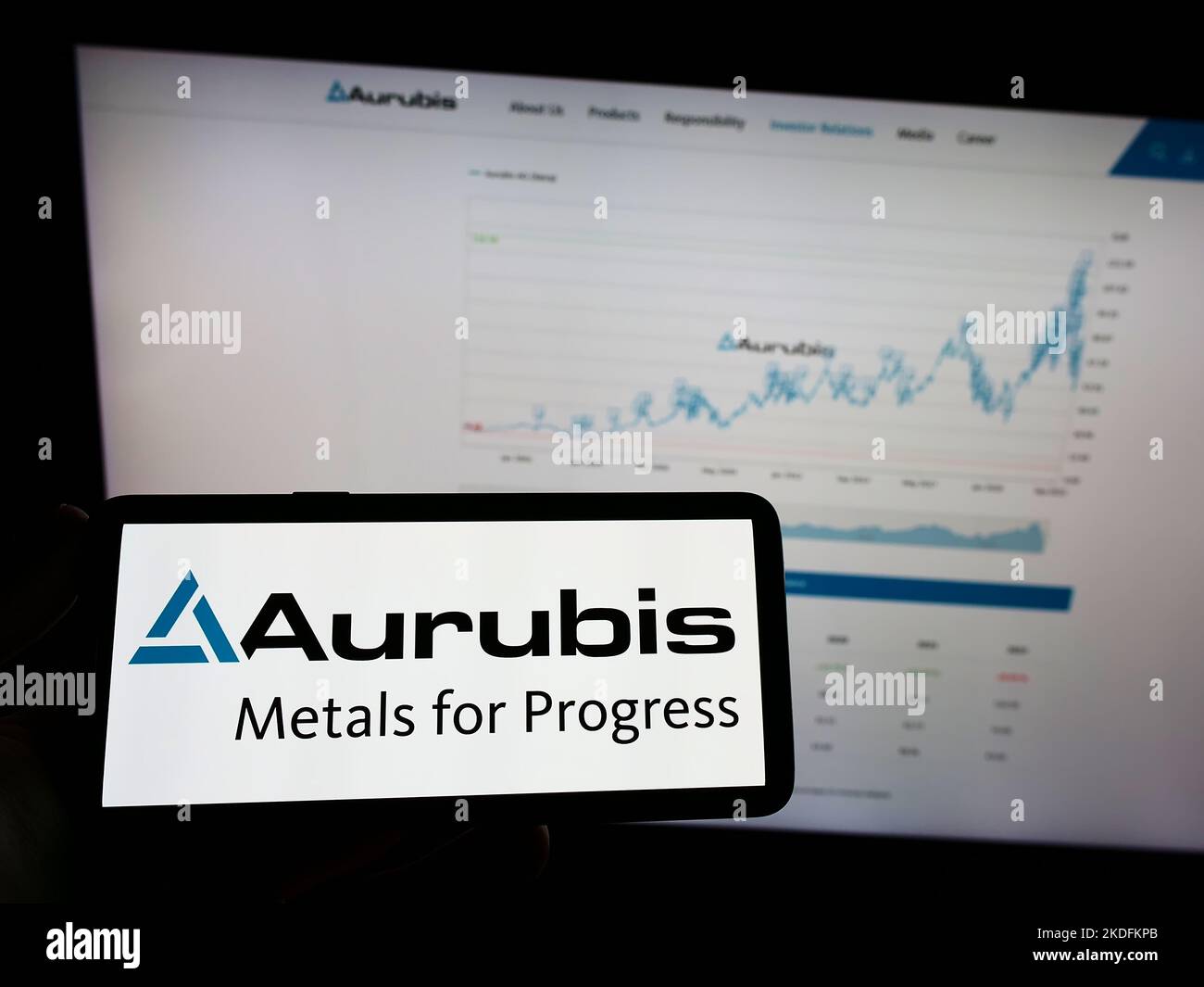 Person holding mobile phone with logo of German copper company Aurubis AG on screen in front of business web page. Focus on phone display. Stock Photo