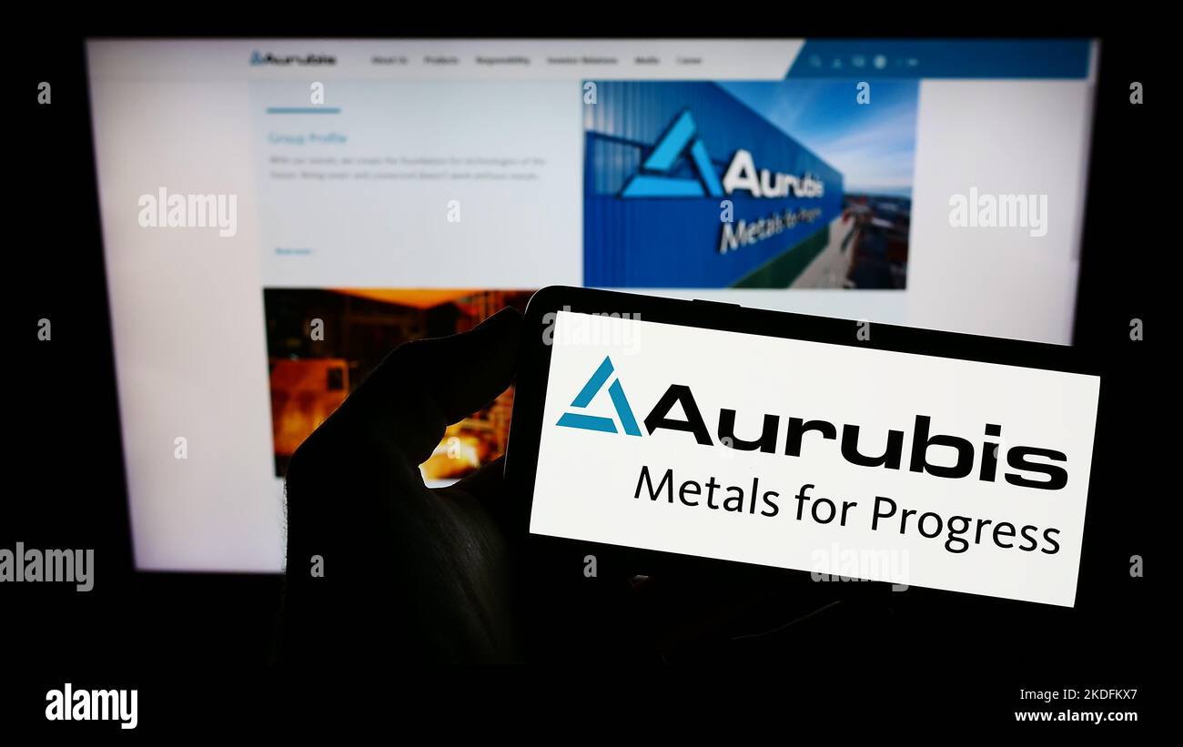 Person holding cellphone with logo of German copper company Aurubis AG on screen in front of business webpage. Focus on phone display. Stock Photo
