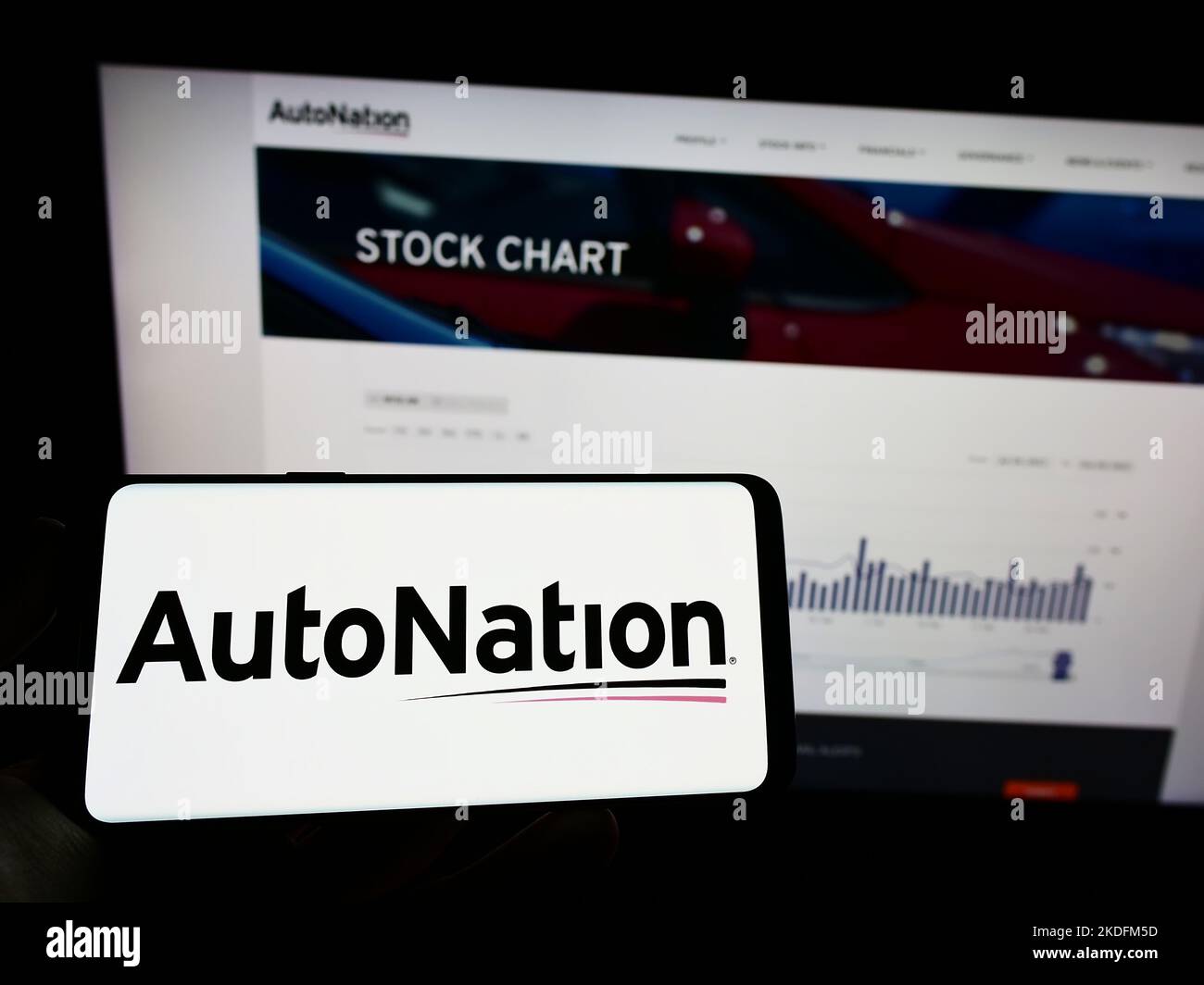 Person holding mobile phone with logo of US automotive retail company AutoNation Inc. on screen in front of web page. Focus on phone display. Stock Photo