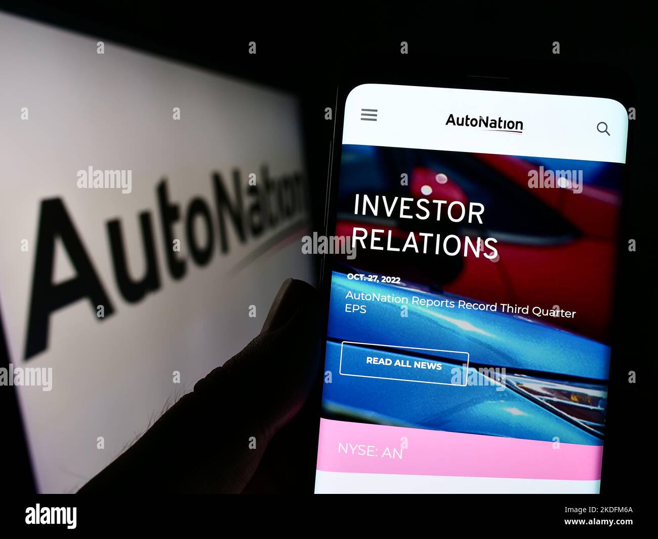 Person holding smartphone with website of US automotive retail company AutoNation Inc. on screen with logo. Focus on center of phone display. Stock Photo