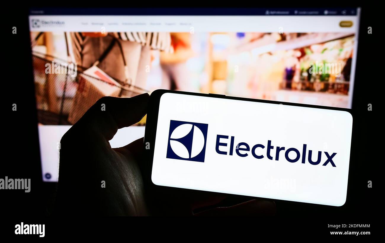 Person holding cellphone with logo of Swedish home appliance company Electrolux AB on screen in front of business webpage. Focus on phone display. Stock Photo