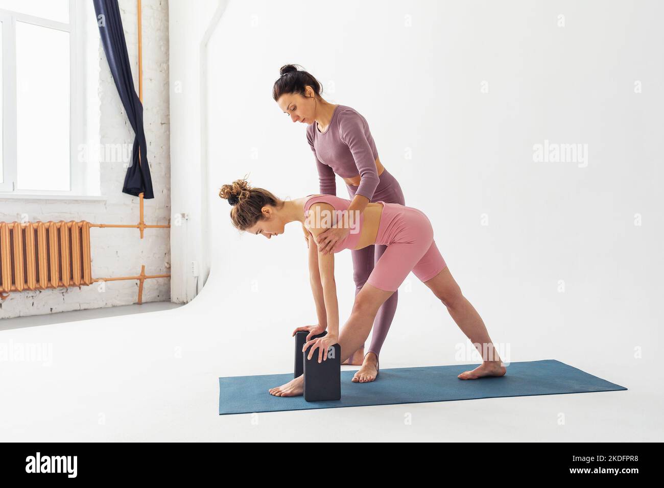 The trainer helps the student to correctly perform the variation of the parshvottanasana exercise, the deep stretching pose, they train in the studio Stock Photo
