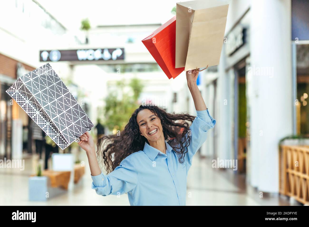 Happy shopper woman looking at camera and smiling, hispanic woman with curly hair dancing and jumping with pleasure, bought gifts on sale, portrait of happy shopping woman. Stock Photo