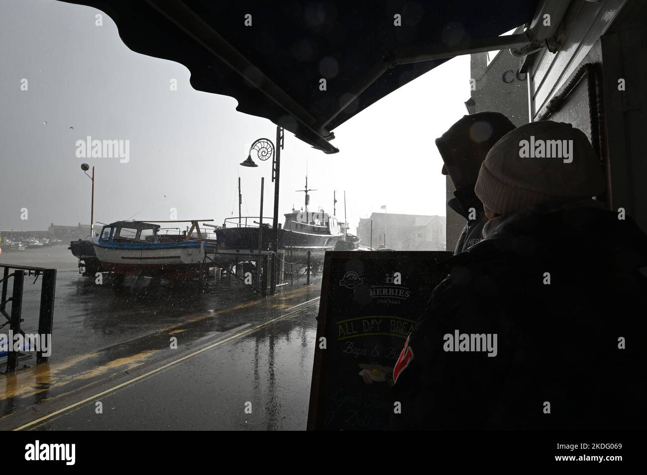 Lyme Resis, UK. 06th Nov, 2022. On a very wet and stormy afternoon of mixed weather conditions two people are seen sheltering under a canopy when a very heavy down pour of rain starts. Picture Credit: Robert Timoney/Alamy Live News Stock Photo