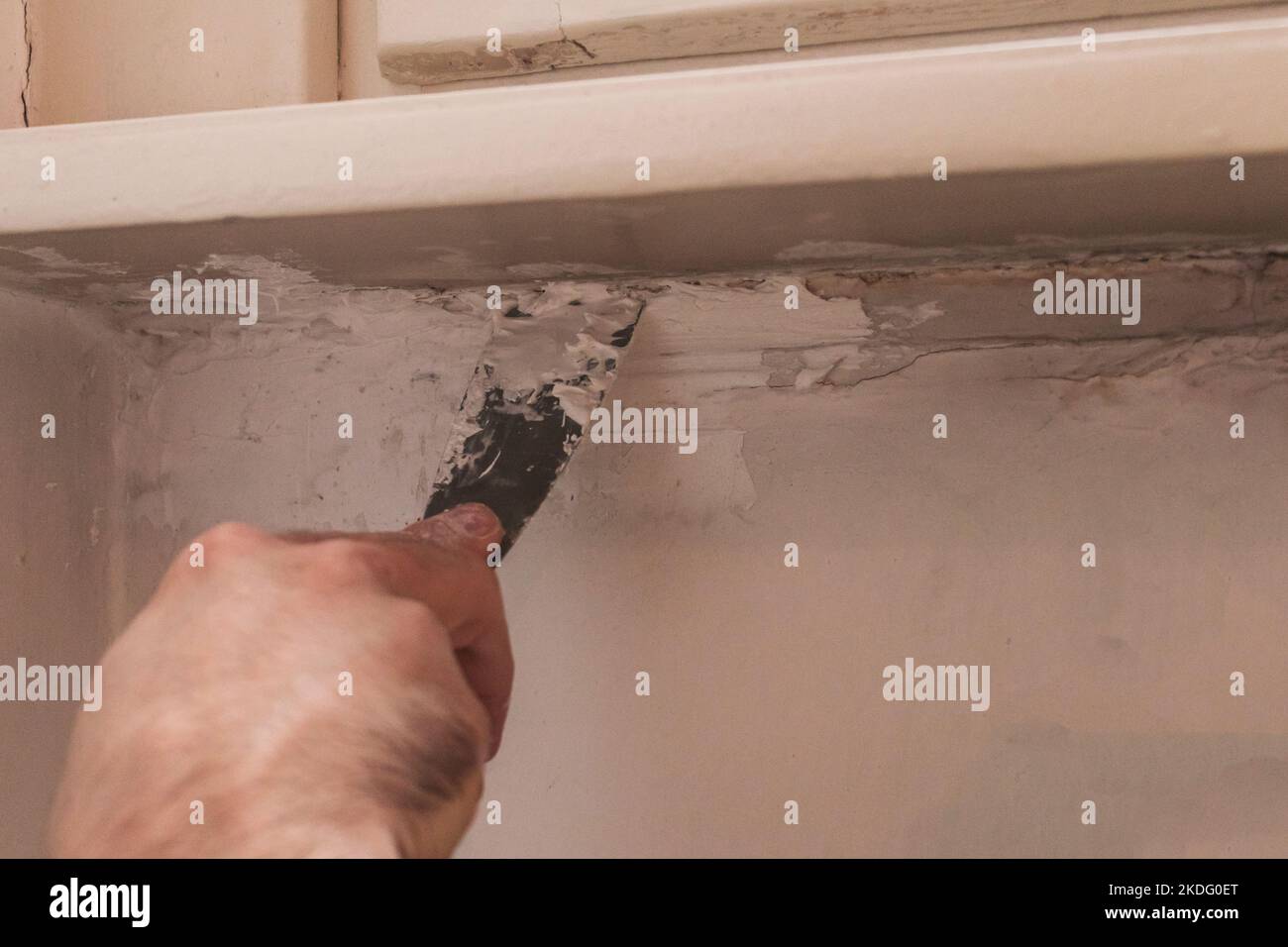 Man hand removing old paint from a wall with a metal spatula. Concept of renovation, home made