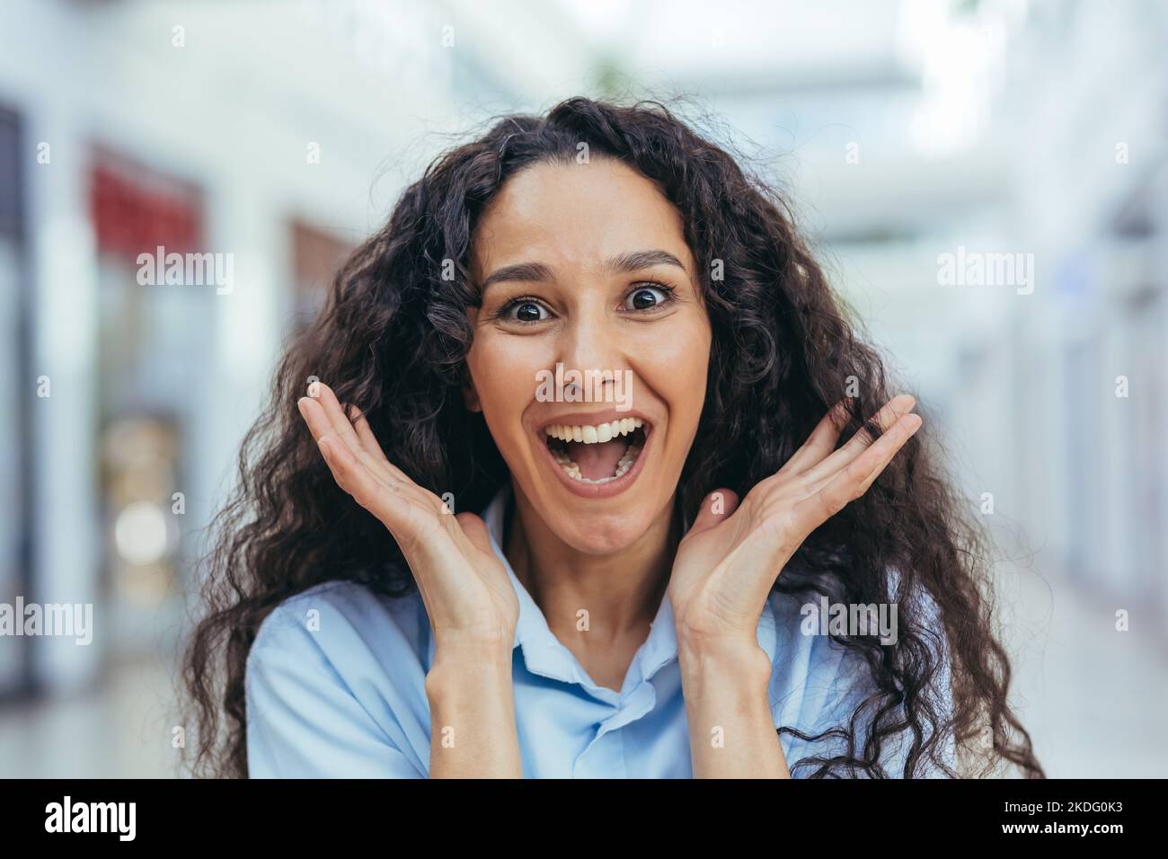 Close-up portrait of female shopper in beehive supermarket, Hispanic woman with curly hair looking at camera with smile. Stock Photo