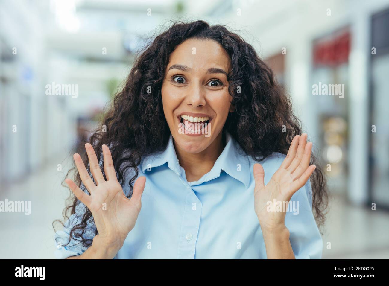 Close-up portrait of female shopper in beehive supermarket, Hispanic woman with curly hair looking at camera with smile. Stock Photo