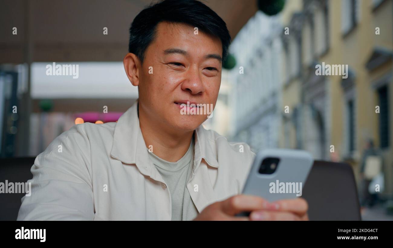 Close-up happy asian man holding mobile phone browsing social network male tourist booking ticket using smartphone sends email message communicates in Stock Photo